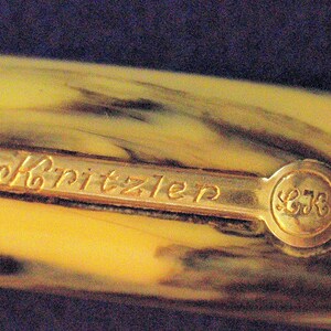 May include: Close-up of a gold-colored pen cap with the inscription "Kritzler" and the number "578" on the side.