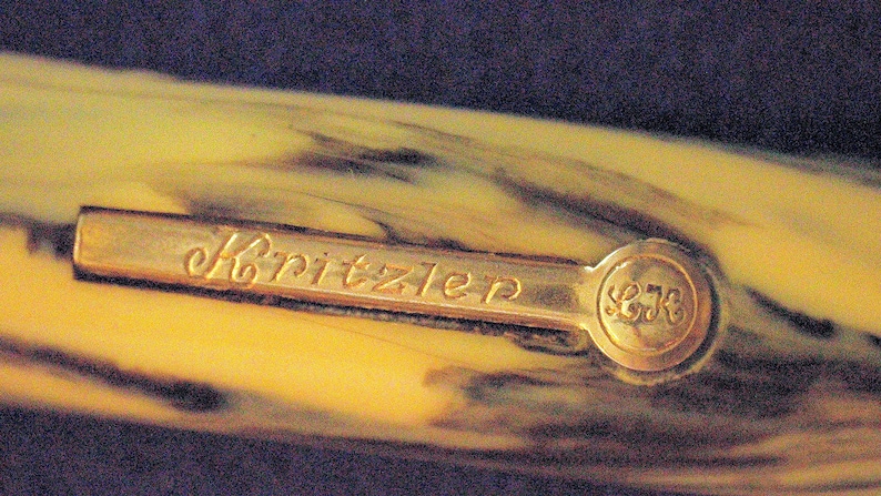 May include: Close-up of a gold-colored pen cap with the inscription "Kritzler" and the number "578" on the side.