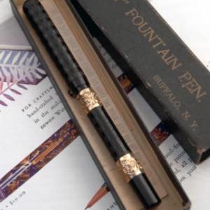 Puede incluir: Una pluma estilogr&aacute;fica negra vintage con detalles dorados, presentada en su caja original. La pluma tiene un cuerpo texturizado y detalles ornamentados. La caja es oscura con el texto "LARKIN" FOUNTAIN PEN" y "BUFFALO, N.Y."