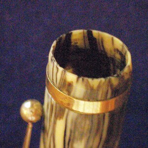 May include: Close-up of the top of a vintage pen with a brown and white marbled design and a gold band around the top.
