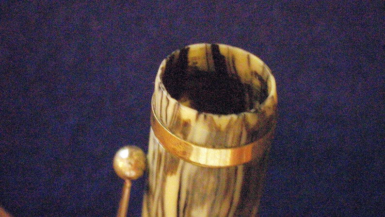 May include: Close-up of the top of a vintage pen with a brown and white marbled design and a gold band around the top.