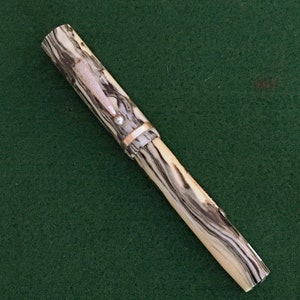 May include: A black and white marbled fountain pen with a gold band and a silver cap. The pen is on a green surface.