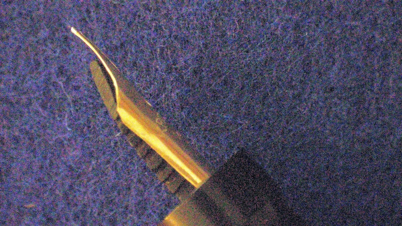 May include: Close-up of a gold-toned fountain pen nib with a fine point.