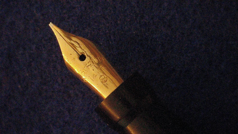 May include: A gold-toned fountain pen nib with a black pen body. The nib has a small hole in the center and the inscription "14K 585" on the side.