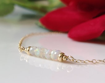 May include: A delicate gold chain bracelet featuring a central row of small, faceted, iridescent white opal beads. The opal beads are flanked by two smooth, round gold beads, with the thin gold chain extending from both sides of the centerpiece.