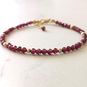 May include: A delicate gold chain bracelet with small, faceted, dark red garnet beads.