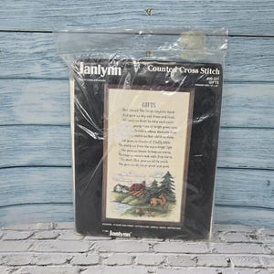 May include: A Janlynn counted cross stitch kit, sealed in plastic. The kit includes a framed landscape scene with a house, deer, and trees, with the word "GIFTS" and a poem printed on the fabric. The kit is labelled "400-321 GIFTS".