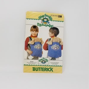 May include: A Cabbage Patch Kids sewing pattern with a yellow, green, and white background. The pattern is for a doll carrier and includes an iron-on transfer. The pattern number is 338. The text "Cabbage Patch Kids" and "Little Bouts de Choux" is printed on the pattern. The text "Butterick" is printed in green on a yellow background at the bottom of the pattern.