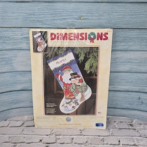 May include: A Dimensions counted cross stitch kit for a Christmas stocking. The design features Santa Claus and a snowman on a blue background. The name "Maria" is stitched on the stocking. The kit includes the design and instructions.