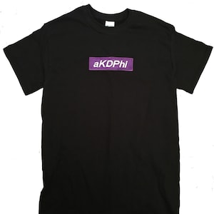 May include: Black t-shirt with a purple rectangle patch that says "akDPhi" in white letters.