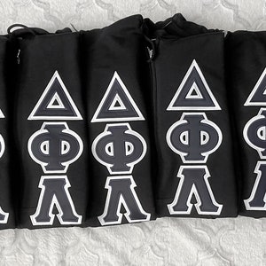 May include: Seven black hooded sweatshirts with white embroidered Greek letters, a triangle, a Phi, and a Lambda on each sweatshirt.