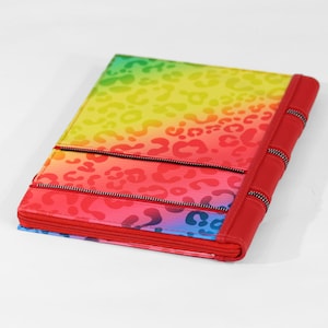 May include: A multi-colored zippered pouch with a rainbow leopard print design. The pouch has three zippered compartments and a red leather spine.