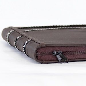 May include: A brown leather zippered case with a decorative silver trim. The case has a zipper closure and is made of a soft, durable material.