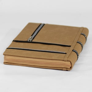 Puede incluir: Un embrague de cuero marrón con cremallera, acentos de cremallera negros y dientes de cremallera plateados. El embrague tiene un detalle de cremallera decorativo en el lateral.