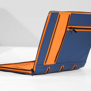 May include: A rectangular blue and orange zippered portfolio case featuring multiple exterior zippered compartments and a bright orange interior lining. The exterior is constructed with alternating blue and orange panels with black zipper hardware.