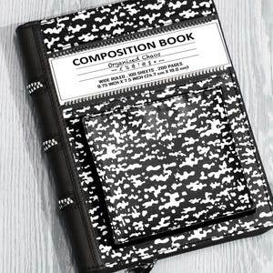 May include: Black and white composition book cover with a zipper closure. The cover features a notebook paper design and the text "COMPOSITION BOOK" and "Organized Chaos". The notebook measures 24.7 cm by 19.0 cm.
