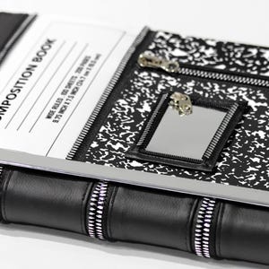 May include: A black and white composition book cover featuring a classic speckled pattern, a rectangular mirror with a zipper border, and a horizontal zipper pocket. The cover displays the text COMPOSITION BOOK, WIDE RULED, 100 SHEETS, 200 PAGES, 9.75 INCH X 7.5 INCH.