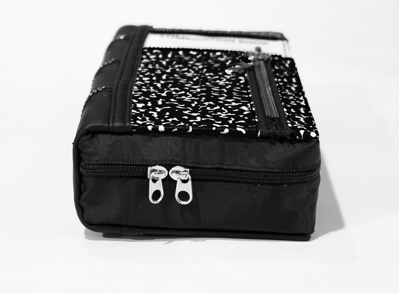 May include: Black zippered pouch with a notebook paper design. The pouch has two zipper closures and a black fabric lining.