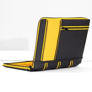 May include: A rectangular zippered portfolio case featuring a bold color-blocked design in black and bright yellow. The exterior includes a horizontal zippered pocket on the front panel, with black fabric accents and yellow piping along the edges.