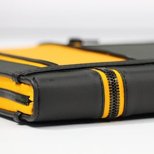 May include: A rectangular zippered case featuring a bold color-blocked design with smooth black panels and vibrant yellow fabric sections. The case is secured with a black zipper track that runs along the edges, contrasting against the yellow fabric.