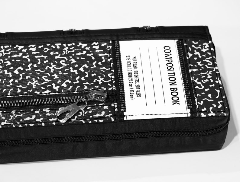 May include: Black composition book with a zipper closure and a white label that reads "COMPOSITION BOOK" and "WIDE RULED. 100 SHEETS. 200 PAGES 9.75 INCH X 7.5 INCH (24.7 cm X 19.0cm)"