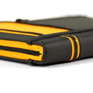 May include: A rectangular black and yellow zippered case featuring a smooth black exterior panel and a vibrant yellow fabric section. The case is secured with a black zipper that runs along the side, providing a contrast against the yellow.