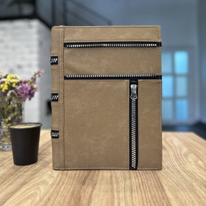 May include: A brown leather journal with a zipper closure and silver accents. The journal has a textured surface and a minimalist design.
