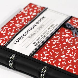 May include: A composition book with a red and white pattern, featuring the text "COMPOSITION BOOK" and "Erika D. Davis." The notebook has a black spine and a zipper closure. The dimensions are 24.7 cm by 19.0 cm.