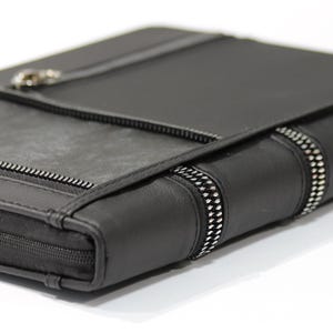 May include: A black leather portfolio with silver zippers and accents. The portfolio has a rectangular shape with a flap closure and a zipper that goes around the edge. The spine has two silver zipper accents.