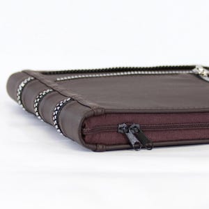May include: A dark brown rectangular zippered case featuring a smooth exterior surface. The case is secured with a dark brown zipper closure and includes decorative silver-toned metallic accents along the side edges and top panel.