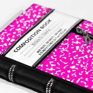 May include: A bright pink and white speckled composition book cover with a black spine and black zipper accents. The white label reads COMPOSITION BOOK, Erika D. Davis, WIDE RULED, 100 SHEETS, 200 PAGES, 9.75 INCH X 7.5 INCH (24.7 cm X 19.0 cm).