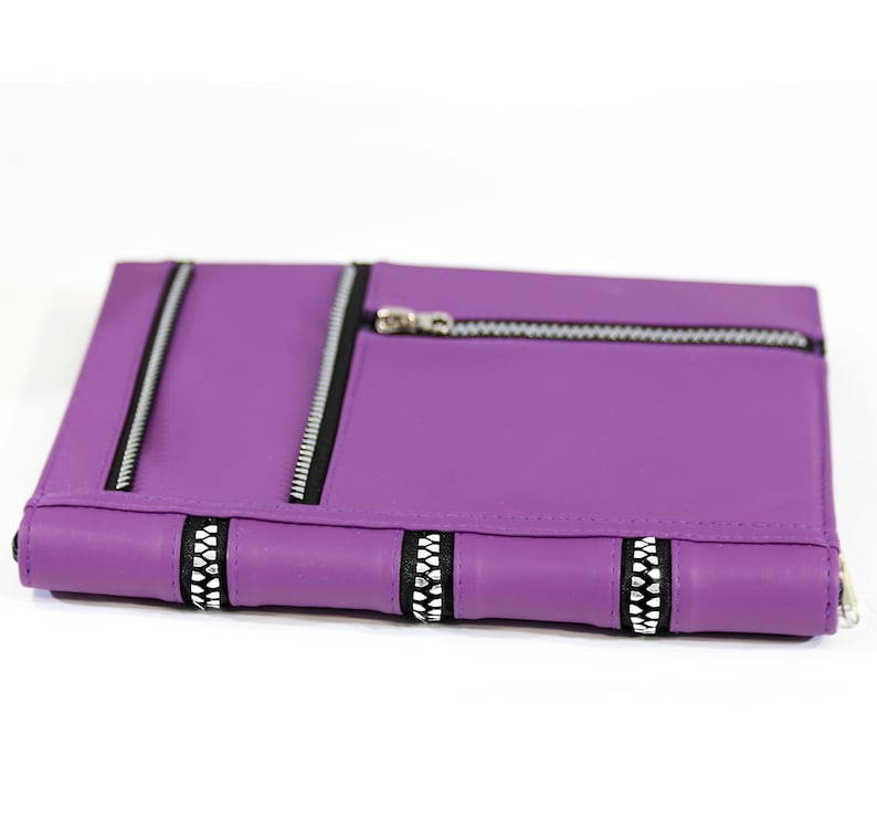 May include: Purple faux leather notebook with zippered pockets and decorative zipper accents.