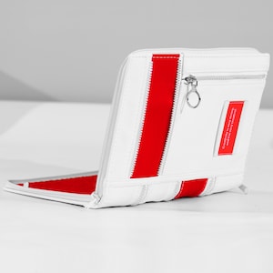 May include: White wallet with a red stripe and zip detail. The wallet has a small red tag with the text "Creativity is very messy, and I'm very creative!" The wallet is open, revealing a red interior.