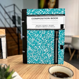 May include: A teal and white speckled composition book with a black spine and zipper accents. The white label reads COMPOSITION BOOK, WIDE RULED, 100 SHEETS, 200 PAGES, 9.75 INCH X 7.5 INCH (24.7 CM X 19.0 CM). It features a vertical zipper closure.
