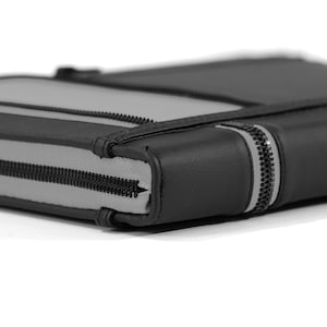 May include: A rectangular black and gray zippered case featuring a smooth black exterior border and a light gray center panel. The case is secured with a black zipper that runs along the side, showing a consistent construction and texture.