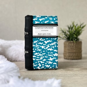 May include: A composition book cover featuring a teal and white speckled pattern with a black spine and two horizontal zippers. The white label reads: COMPOSITION BOOK, silverskylake, WIDE RULED, 100 SHEETS, 200 PAGES, 9.75 INCH X 7.5 INCH.