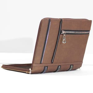 May include: A brown rectangular portfolio case featuring a smooth matte finish. The exterior is decorated with three vertical black and silver zippers and one horizontal black and silver zipper with a silver metal pull tab on the upper right side.