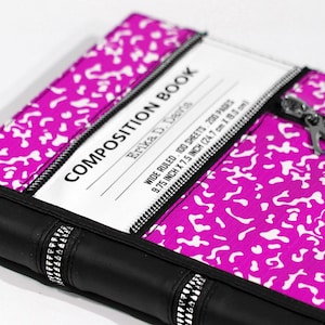 May include: A bright pink and white speckled composition book cover featuring a black spine with silver zipper accents. The white label area displays the text COMPOSITION BOOK, ERIKA D. DAVIS, WIDE RULED 100 SHEETS 200 PAGES, and 9.75 INCH X 7.5 INCH.