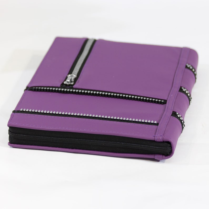 May include: A purple leather zippered notebook with silver accents and a black zipper.