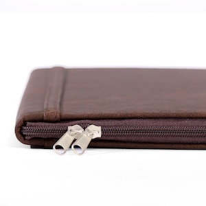 May include: A close-up of a brown zippered case. The case is rectangular with rounded corners and a dark brown zipper. The zipper pulls are silver. The case appears to be made of a soft, textured material.