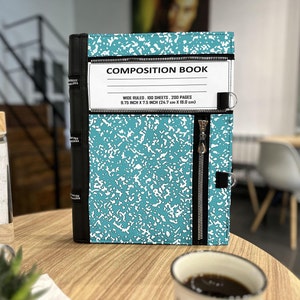 Puede incluir: Un cuaderno de composición azul turquesa con una cubierta de cuero negro y cierre de cremallera. El cuaderno tiene un patrón moteado blanco y el texto "COMPOSITION BOOK" y "WIDE RULED. 100 SHEETS. 200 PAGES 9.75 INCH X 7.5 INCH (24.7 cm X 19.0 cm)" impreso en la portada.