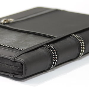 May include: Black leather portfolio with silver zippers and accents. The portfolio has a flap closure and a zipper that goes around the entire case. The edges are detailed with silver studs.