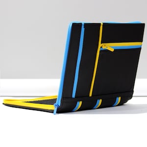 May include: A black portfolio case featuring bright blue and yellow zipper accents. The exterior includes vertical zipper detailing and a horizontal zippered pocket with a matching yellow pull tab. The interior lining is black with a yellow border.