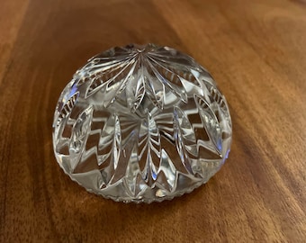 May include: A clear, cut-glass bowl with a rounded shape. The bowl features a detailed pattern of vertical and curved cuts, creating a textured surface. The bowl is sitting on a wooden surface.