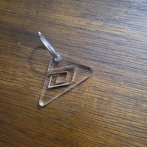 May include: Clear acrylic keychain with a geometric design. The keychain features a triangular shape with a spiral design inside. A silver metal keyring is attached to the top of the keychain.
