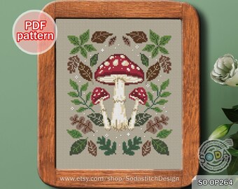 Puede incluir: Patrón de punto de cruz con un hongo rojo y blanco con hojas verdes y bellotas marrones. El patrón se titula "SO-OP264" e incluye la dirección del sitio web "www.etsy.com/shop/SodastitchDesign".