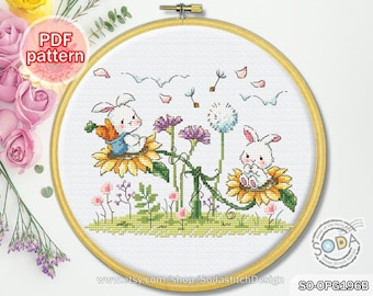May include: Cross stitch pattern featuring two white bunnies sitting on sunflowers with a dandelion and other flowers in the background. The pattern is in a round hoop and the text "PDF pattern" is in the top left corner.