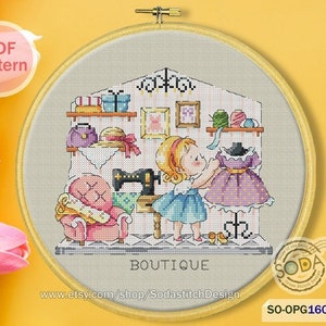 以下が含まれることがあります： 青いドレスを着た女の子が、ミシン、ピンクの椅子、紫のドレスを着たマネキンがあるブティックに立っているクロスステッチパターン。画像の下に「Boutique」という文字があります。