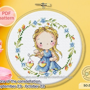 May include: A cross-stitch pattern featuring a cartoon illustration of a girl holding a scale, surrounded by a wreath of flowers. The text "Libra of the constellation September 23 - October 22" is below the image. The text "SODA" is in a circle with a star in the bottom right corner of the image.