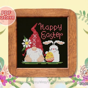 Könnte beinhalten: Kreuzstichmuster mit einem Zwerg mit roter Mütze und einem weißen Hasen, der ein Osterei hält. Die Worte "Happy Easter" sind in Rosa gestickt. Das Design ist in einem Holzrahmen gerahmt. Die Worte "PDF pattern" befinden sich in der oberen linken Ecke.
